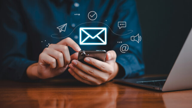 Person holding smartphone with email and communication floating above person, smartphone, email, communication, phone, mobile, laptop, computer, desk, table, wood, hands, fingers, screen, digital, mes