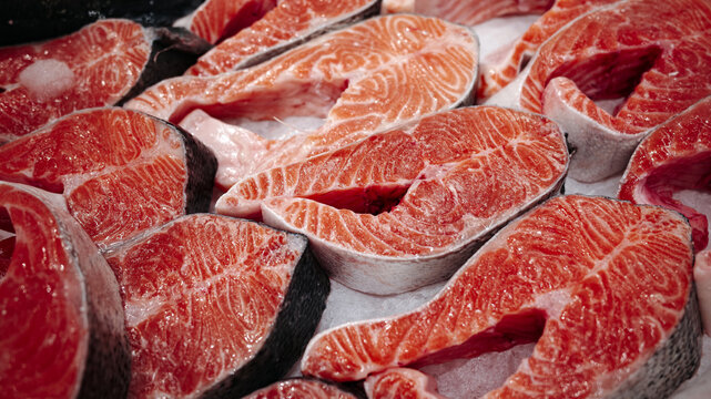 Fresh raw salmon steaks on display, bright orange fish meat with marble texture and skin, ready for cooking, seafood market background.