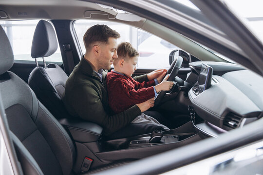 Father and son sitting in car at dealership, man teaching boy driving, family bonding over new auto purchase