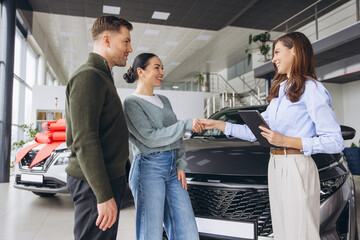 Naklejka premium Happy couple concluding purchasing a new automobile, shaking hands with professional sales agent in a bright car dealership showroom