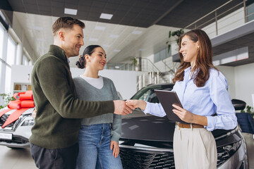 Naklejka premium Couple celebrating new car purchase in dealership, shaking hands with saleswoman and finalizing a deal