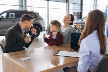 Family celebrating successful car purchase at modern dealership, receiving new car keys from...