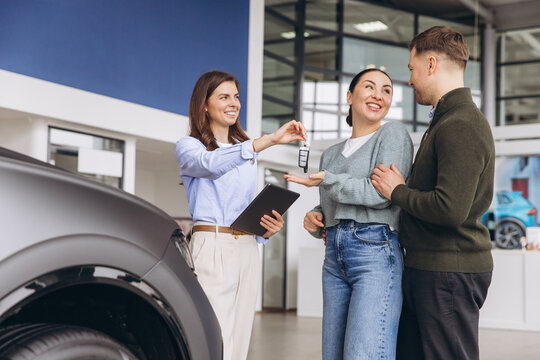 Saleswoman handing over car keys to a happy young couple buying a new vehicle in an automotive showroom
