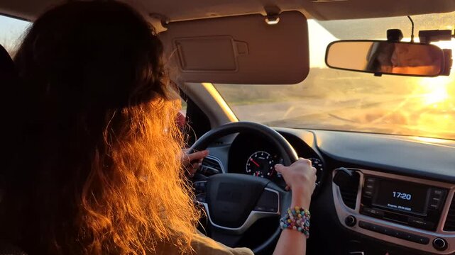 Driving, travel, sunset. Woman driving car interior during golden hour, long road trip commuter journey.