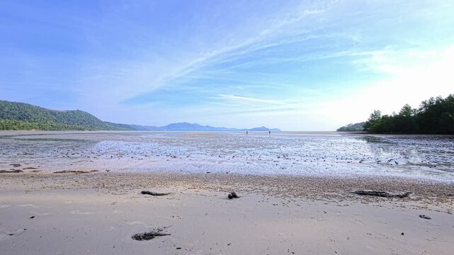 Wide intertidal beach with two distant people in Thailand under morning light