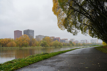 Fototapeta premium Autumn in the city in Moscow. Cityscape with the modern multi-story residential buildings reflected in a pond in autumn. Contemporary urban development, innovative architectural solutions