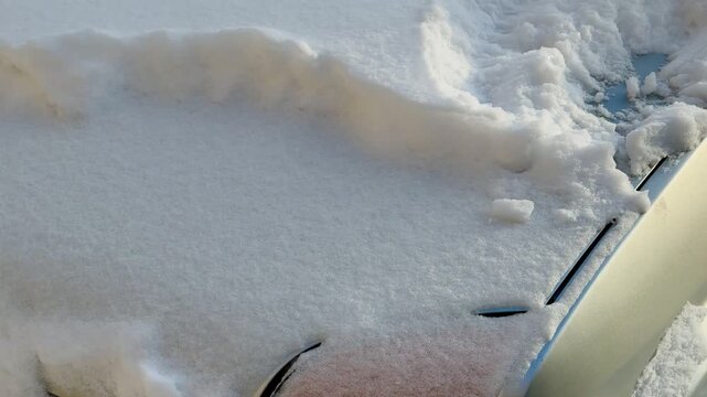 The snow-covered passenger car is completely covered with snow. The windscreen wipers, exterior mirrors, and door handles are all frozen with ice and covered with snow. Severe winter weather.