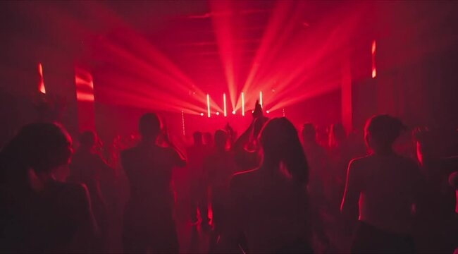 Crowd dancing at a nightclub with red lighting and people enjoying the music event