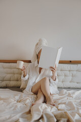 Lifestyle Portrait Of Woman Sitting In Bed With Towel On Head Holding Mug And Notebook