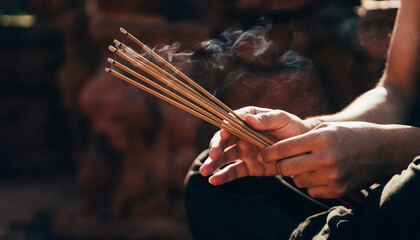Person holding and lighting incense sticks with smoke rising.