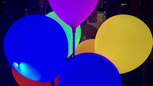 Slow zoom out footage of colorful glowing LED balloons in dark indoor environment.