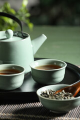 Tray with teapot, cups of tea and dry leaves on green table outdoors