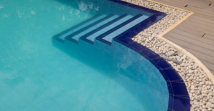 Abstract view of modern swimming pool corner with submerged steps and pebble edge