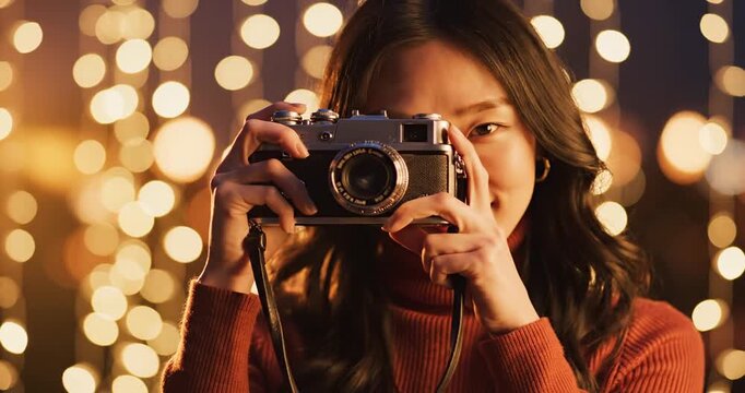 Young woman smiling while holding a vintage camera, illuminated by festive lights at night