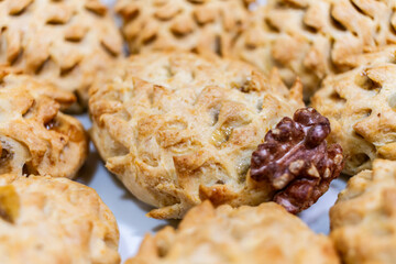 Close-up of freshly baked mini pies with golden flaky crust and cutout pattern, arranged on a tray with soft focus background. One pastry has a walnut piece, ready-to-serve homemade dessert.