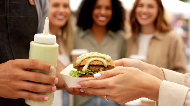 Street food vendor in apron adding green sauce to a gourmet veggie burger being received by customers, concept for fast food menu, healthy eating promotion and casual dining experience