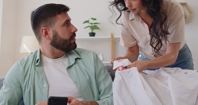 Couple confrontation and conflict over red lips marks on husbands office shirt. Angry wife showing lipstick stain evidences of adultery and betrayal, man in confusion denying infidelity and cheating