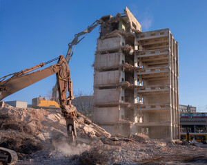 Excavator demolishing a concrete high-rise building at an urban demolition site
