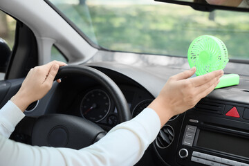 Young woman using mini electric fan in car