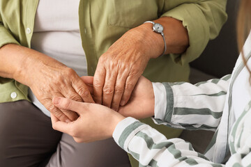 Fototapeta premium Young woman with grandmother holding hands at home, closeup. Care concept