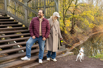 Obraz premium Adult Man And Woman Walking Small Dog Near Wooden Staircase In Autumn Park