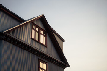 Traditional Icelandic house with red window frames and corrugated iron wall under sunset sky