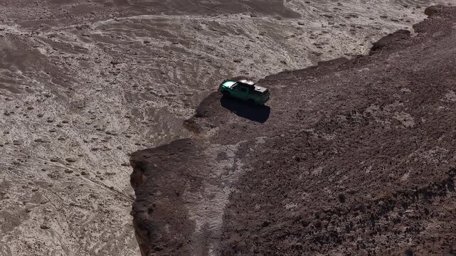 Aerial view of a pickup truck driving on a mountain cliff edge of Bozjyra