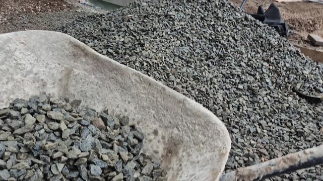 Slow motion close-up of construction workers shoveling bedding gravel into a wheelbarrow.