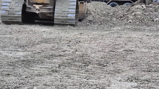 Slow motion low angle rear view of a bulldozer crawler tracks leveling soil on rough terrain.