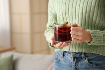 Woman holding glass cup of hot mulled wine at home, closeup