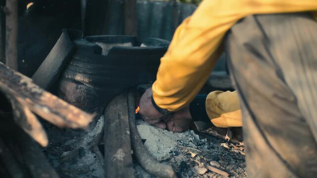 Close up of person tending an outdoor fire for cooking or heating in a rustic setting with natural light