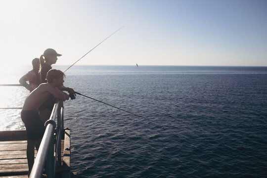 Serene silhouette of teenage children / siblings fishing together on jetty