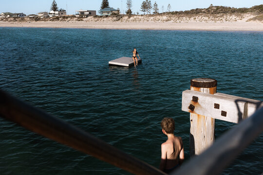 Boy waiting to jump off jetty while watching girl in the distance