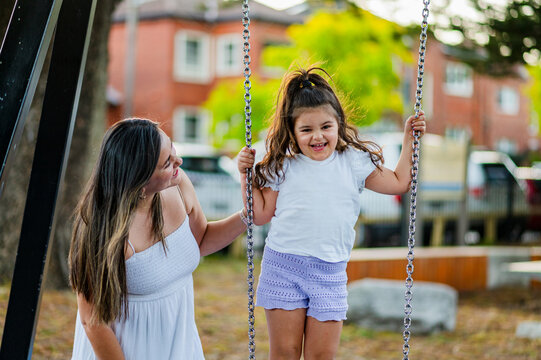A young girl enjoys swinging with her mother in a park setting while playing in the afternoon