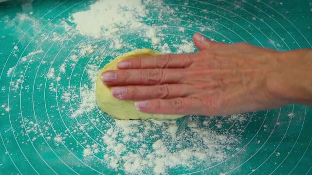 A woman is rolling out dough into a flatbread on a silicone mat using a rolling pin. This is a traditional method of preparing food from yeast dough, following family recipes.