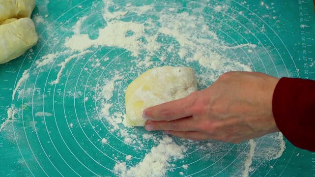 A woman is rolling out dough into a flatbread on a silicone mat using a rolling pin. This is a traditional method of preparing food from yeast dough, following family recipes.