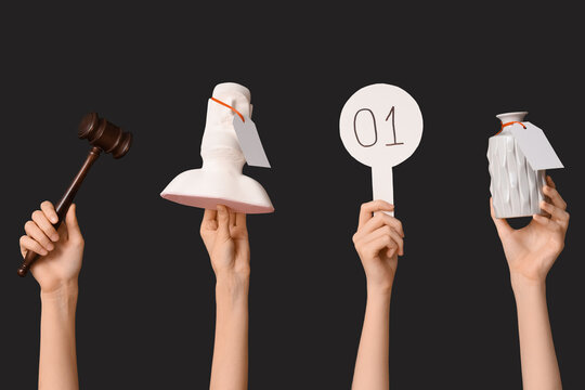 Female hands with auction paddle, gavel and antique items on dark background