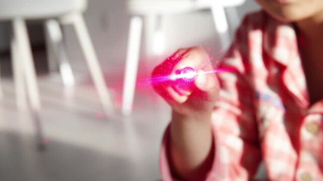 Child's Hand Operating a Toy Laser Pointer with a Bright Red Beam