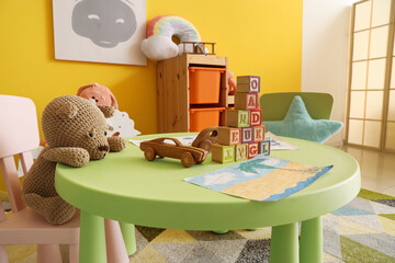 Toy table with wooden cars, cubes and paintings in kindergarten, closeup