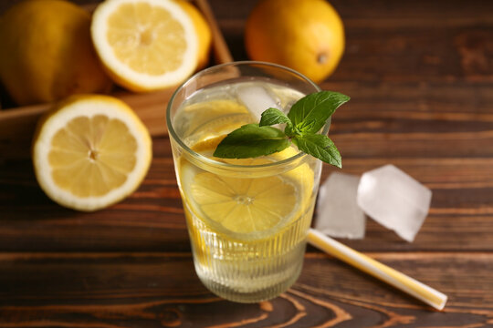 Glass of fresh lemonade with mint and ice cubes on wooden background