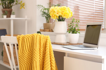 Comfortable workspace with modern laptop and yellow narcissus flowers on white desk, closeup