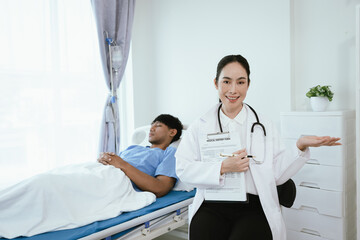 Obraz premium Female doctor reviewing medical records on a clipboard while a male patient rests in a hospital bed during inpatient care.