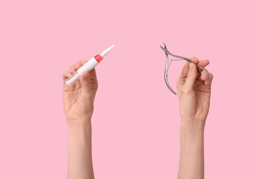 Female hands with cuticle oil pen and nail cutter on pink background