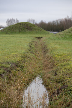 Drainage ditch with standing water leading to a grassy mound