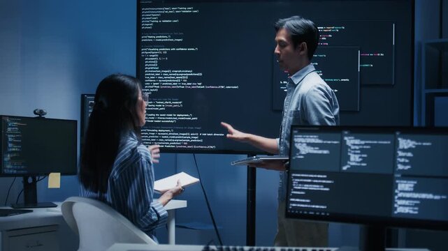 Asian Male software engineer pointing at source code on a large screen during a tech team meeting, explaining Code on the Screen, Discussing on coding task, New software development project in office.
