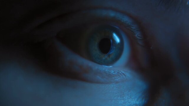 Close-up of an eye staring intently at a phone screen with a reflection of social media or news feeds in the pupil at night under blue light. Insomnia, sleep disorders, and doomscrolling. 
