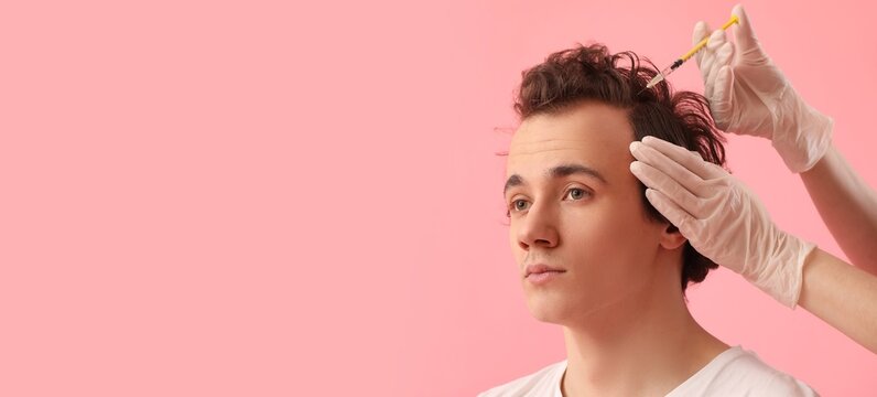 Young man with hair loss problem receiving injection on pink background with space for text