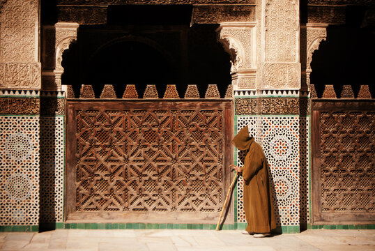 Man walking past a traditional wooden lattice screen in the courtyard of the Medersa Bou Inania in Fez, Morocco