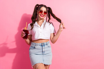 Bright casual fashion portrait of a young woman with pink background holding juice and wearing...