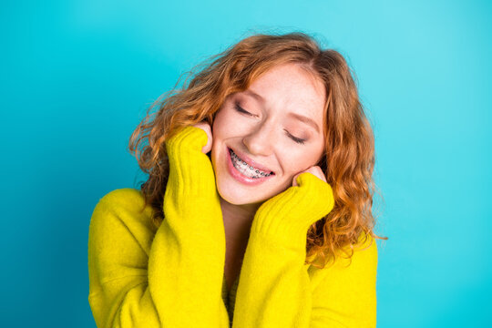 Joyful redhead girl in a bright yellow sweater smiles with braces against a vivid blue background